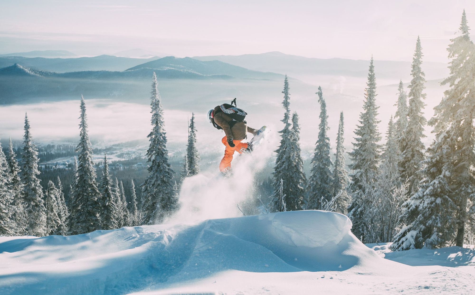 Snowboarder jumping through fresh powder between snowy trees